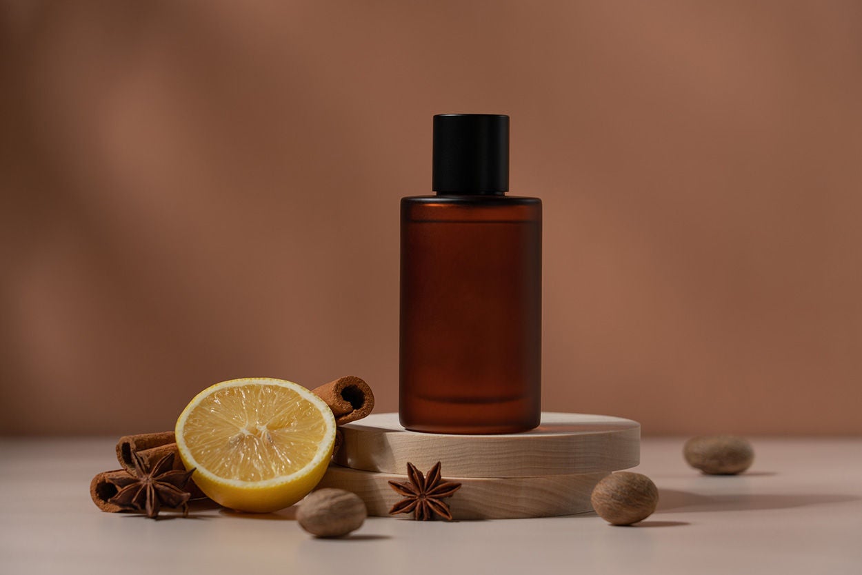 Amber glass perfume bottle on the podium with spices of cinnamon, nutmeg and citrus. Brown trendy beauty background with copy space